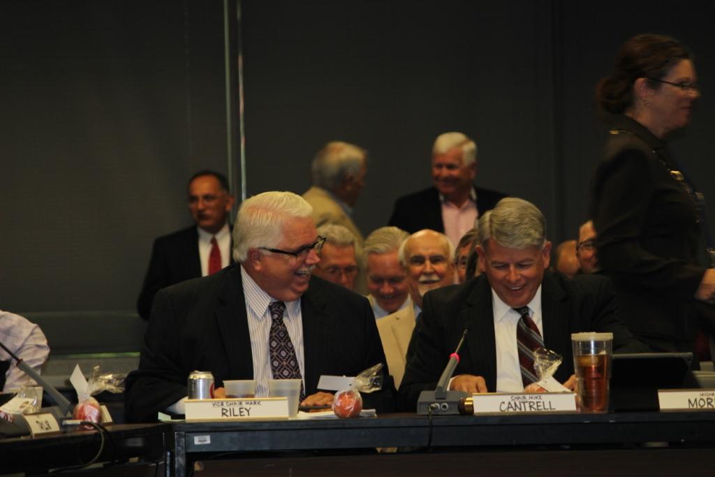 Parker County Judge Mark Riley, Vice Chairman of the Regional Transportation Council and Dallas County Commissioner Mike Cantrell, RTC Chairman, share a laugh after Judge Riley gives each council member a Parker County Peach at the July meeting of the RTC